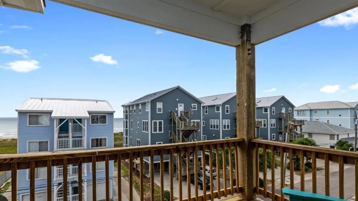 A tranquil view from the deck, featuring blue sky, nearby buildings, and the outdoor deck railing. The perspective captures the feeling of openness and connection to the Atlantic Ocean, highlighting the expansive view available from the deck area.