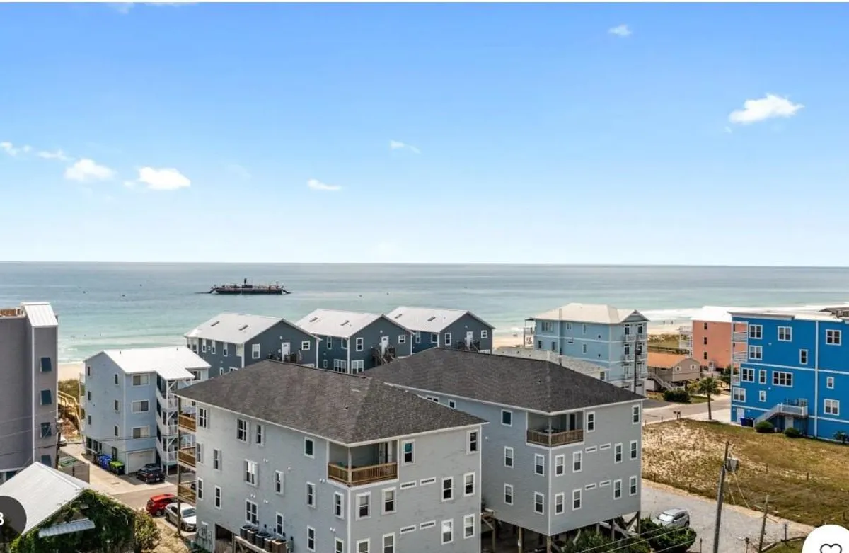 The hero image showcases a tranquil, sweeping ocean view from the condo's deck, with vibrant beachfront buildings in the foreground and the shoreline just steps away. The sun is low, casting a warm glow over the water, hinting at beautiful sunsets and serene mornings. The scene invites thoughts of relaxing days by the shore, scenic beach walks, and the lively spirit of the boardwalk nearby.