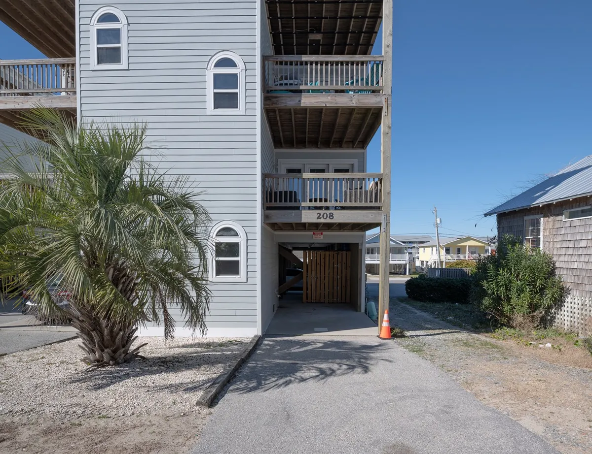 This image shows a relaxed exterior view of the building facade with a palm tree, visible balcony, and adjacent parking area where vehicles can be seen parked. The casual vibe hints at easy access and welcoming arrival.