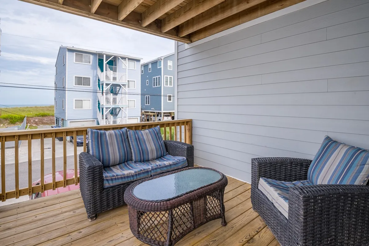 An inviting exterior seating area featuring wicker chairs and a glass-topped table, with views of nearby buildings. The cozy setup hints at spaces for socializing, enjoying a drink, or starting the day outdoors.
