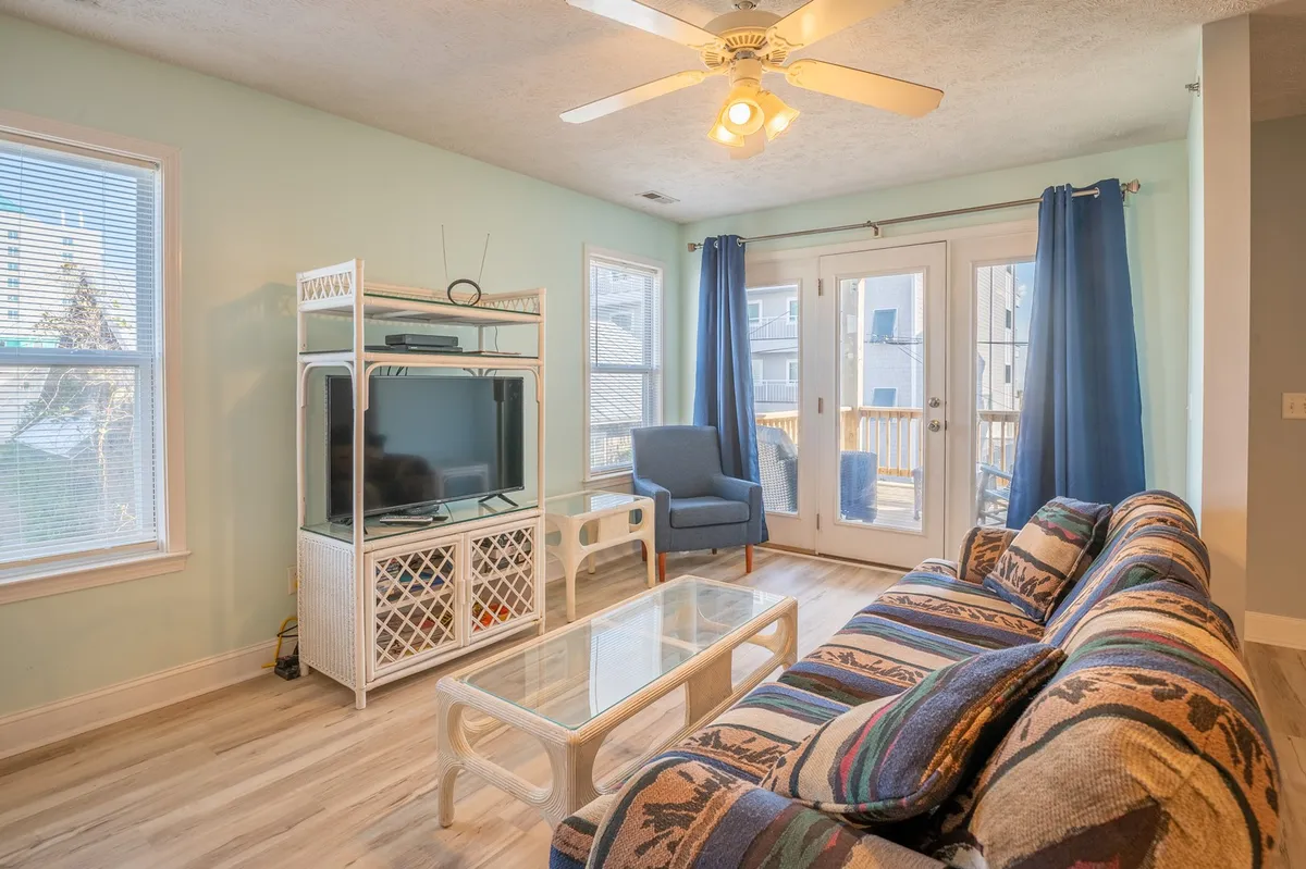 A bright, inviting living room with a comfy sofa, television, and sunlight streaming through window curtains. The space is arranged for relaxation and casual socializing, encouraging guests to unwind after a day of adventure or enjoy morning light together.