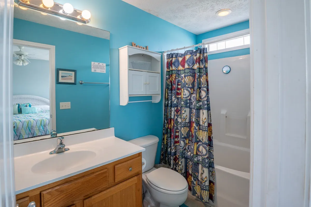 A sparkling clean hallway bathroom with vibrant blue walls, a colorful shower curtain, and a fresh white vanity. The mood is bright and inviting, making morning routines or evening wind-downs a pleasure.